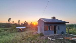 a small house in a field with the sunset in the background at Vertiente escondida in Villa Yacanto