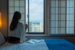 a woman sitting on a bed looking out the window at Hotel Resol Trinity Kyoto in Kyoto +123 photos