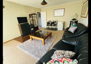 a living room with a black leather couch and a table at Private 2-Bedroom Suite in 3-Bedroom House in Auckland