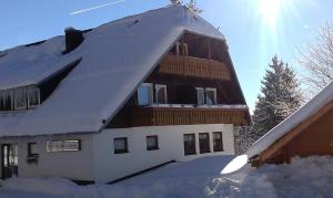 une maison recouverte de neige avec le soleil derrière elle dans l'établissement Schwarzwaldgasthaus Salenhof, à Titisee-Neustadt