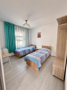 two beds in a bedroom with green curtains at Jibek Murok in Bosteri