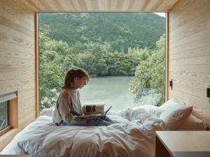 Eine Frau sitzt mit einem Laptop vor einem Fenster auf einem Bett. in der Unterkunft allbeans KOCHI in Kami + 17 Fotos