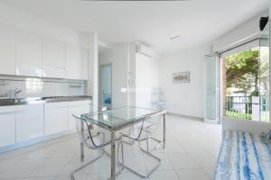 a white kitchen with a glass table and chairs at Residence Playa Grande Immobiliare Pacella in Lido di Jesolo