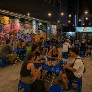 a group of people sitting at tables with pizza at Bluedot Poshtel in Seoul