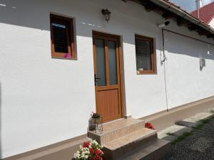 a white house with a wooden door and some flowers at Viktória central apartman in Odorheiu Secuiesc