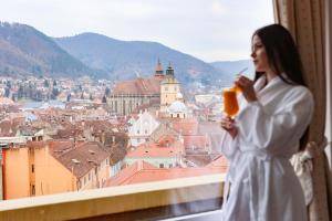 a woman in a white dress holding a glass of wine looking out a window at Hotel Aro Palace in Braşov +51 photos