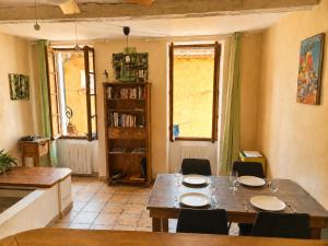 a dining room with a table and chairs and two windows at Le logis de la Fontaine in Ceyreste