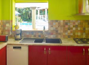 a kitchen with red cabinets and a sink and a window at Appartement spacieux avec jardin et piscine à Lamentin, 97 m² in Lamentin