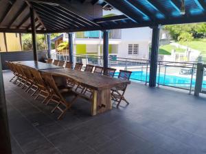 a wooden table and chairs on a patio with a pool at Appartement spacieux avec jardin et piscine à Lamentin, 97 m² in Lamentin