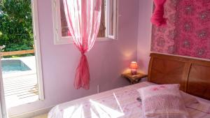 a bedroom with a bed and a window with pink curtains at Maison charmante Le Moule + piscine in Le Moule