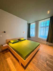 a bedroom with a bed with green sheets and a window at Tussen Muur en Markt in Ieper +1 photo