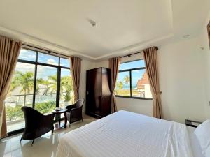 a bedroom with a bed and chairs and windows at Hila Hotel Vạn Ninh in Vạn Ninh