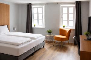 a bedroom with a bed and a chair and two windows at Dahlbrucher Hof in Hilchenbach