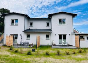 a white house with chairs and tables in a yard at Ferienwohnungen Soldanski in Loddin