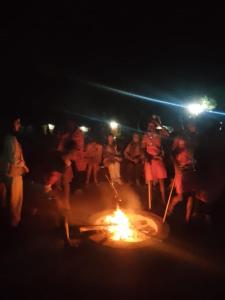 a group of people standing around a fire at night at Giraffe Hills Mara Camp in Ololaimutiek