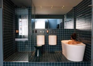 a blue tiled bathroom with a woman sitting in a tub at Maison Arya in Brussels