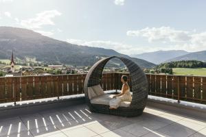 a woman sitting in a wicker chair on a balcony at Hotel Fameli in Valdaora