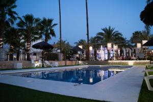a swimming pool with umbrellas and palm trees at Hacienda Guadalquivir in Córdoba