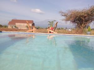 a swimming pool with two chairs and a house at I love Amboseli in Kimana