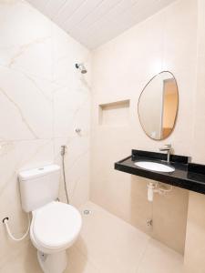 a white bathroom with a toilet and a mirror at Pousada Milagres in Canindé