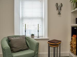a living room with a green chair and a window at Fifie Cottage in Johnshaven