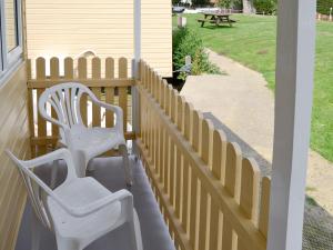 two white chairs on a porch with a fence at Halcyon - Uk12696 in Stalham