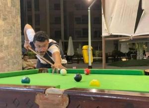 a man is playing pool on a pool table at grand hills in Dawwār ‘Abd Allāh