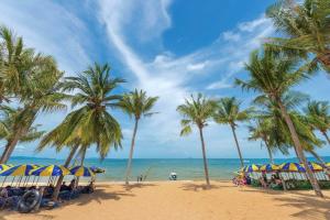 a beach with palm trees and chairs and the ocean at Sunny Beach Residence in Jomtien Beach