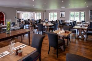 a restaurant with wooden tables and chairs and windows at The Slaughters Country Inn in Lower Slaughter
