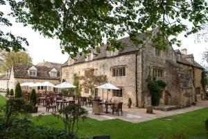 a large stone building with tables and umbrellas at The Slaughters Country Inn in Lower Slaughter
