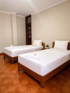 two beds in a room with white walls and wooden floors at La Posada Del Pajarito in Yurimaguas