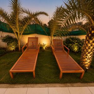 two wooden benches sitting on the grass with palm trees at Amrit Farm in Rāi