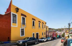 a yellow building with cars parked on the side of a street at Hotel Departamentos Suites in Guanajuato