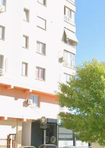 a white building with a tree in front of it at Cozy Apartment Astiri in Tirana
