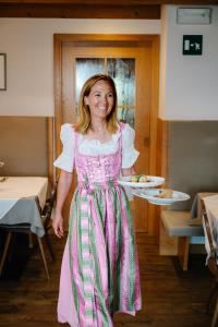 a woman in a pink dress holding a plate of food at Hotel Wiesl in Collepietra