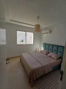 a bedroom with a bed with a blue headboard and a window at Le charment in Sukrah