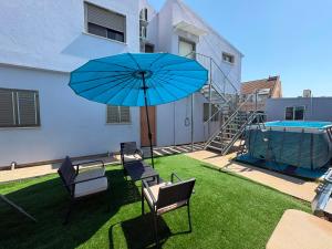 a patio with a blue umbrella and chairs and a pool at Rest&breath in Nir Yafe