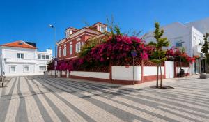 a building with pink flowers on the side of a street at Vila Olivença in Costa da Caparica