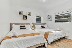 two beds in a bedroom with white walls and windows at New Casa Eva Turfed Pool 5Br in Hallandale Beach +25 photos