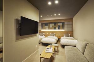 a living room with two beds and a flat screen tv at KURASHIKI Station HOTEL 和奏 in Kurashiki