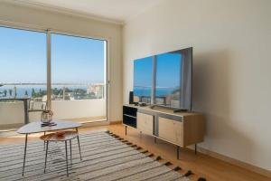 ein Wohnzimmer mit Fernseher und großen Fenstern in der Unterkunft Sunflower Ocean View Apartment With Pool & Parking in Caniço