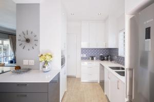 a white kitchen with white cabinets and a vase of flowers at Quiet Garden Flat Near Kenilworth Centre in Cape Town