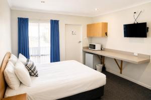 a bedroom with a bed and a desk with a microwave at Busselton Motel in Busselton
