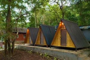 a group of three wooden houses with roofs at Rain Forest Jungle Stay in Kurandi