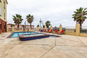 a swimming pool with red chairs and palm trees at Comfort Suites Galveston Cruise Port Area - Beachside in Galveston