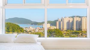 a bedroom with a view of a city from a window at Geoje Forest-Morning Spa Pension in Geoje