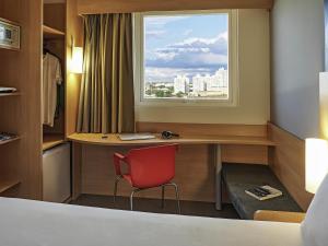a room with a desk with a window and a red chair at ibis Londrina Shopping in Londrina