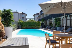 a swimming pool with chairs and a table and an umbrella at Auckland Rose Park Hotel in Auckland