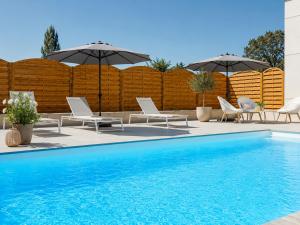 a pool with chairs and umbrellas next to a fence at Mercure Lyon Genas Eurexpo in Genas