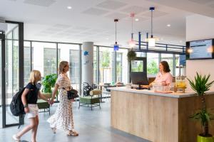two women walking through an office lobby with a reception counter at ibis Styles Angouleme Centre in Angoulême